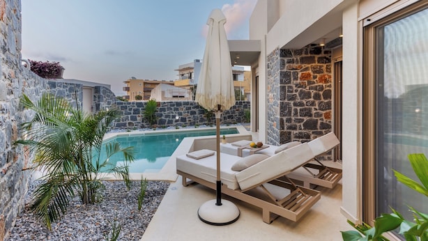 A poolside area with a lounge chair and umbrella, surrounded by stone walls and plants.