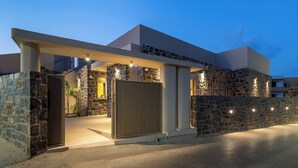A modern house with a stone facade, a large wooden gate, and a covered driveway. - Numa Villas - Villa Taupe, by Estia (Malia)
