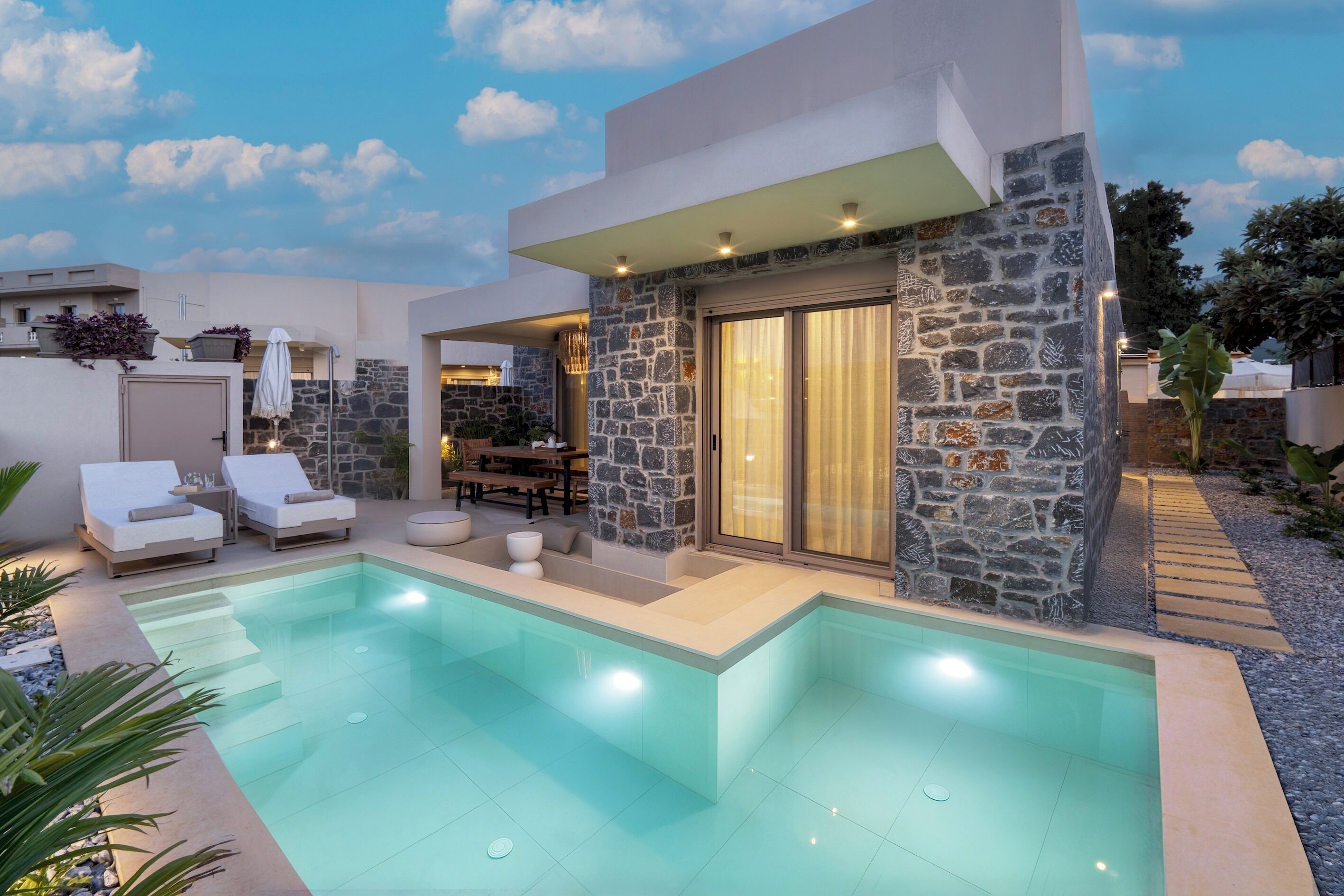 A modern house with a swimming pool, stone walls, and outdoor seating.