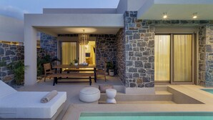 A modern outdoor pool area with stone walls, a dining set, and lounge seating. - Numa Villas - Villa Taupe, by Estia (Malia)