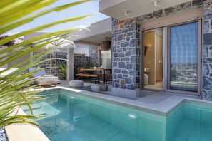 A modern outdoor pool area with stone walls and a glass door leading to a room. - Numa Villas - Villa Taupe, by Estia (Malia)