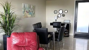 Un salon moderne avec un canapé en cuir rouge, un coin repas comprenant une table et des chaises, une plante en pot et un tableau accroché au mur.