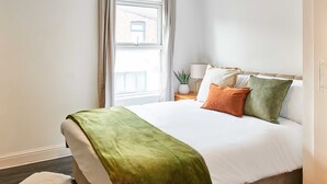 A neatly made bed with a green blanket, white pillows, and a view of a building through a window. - Host Stay Bishop House (Liverpool)