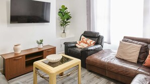 A modern living room with a flat-screen TV, a leather sofa, a wooden coffee table, and a potted plant. - Host Stay Bishop House (Liverpool)