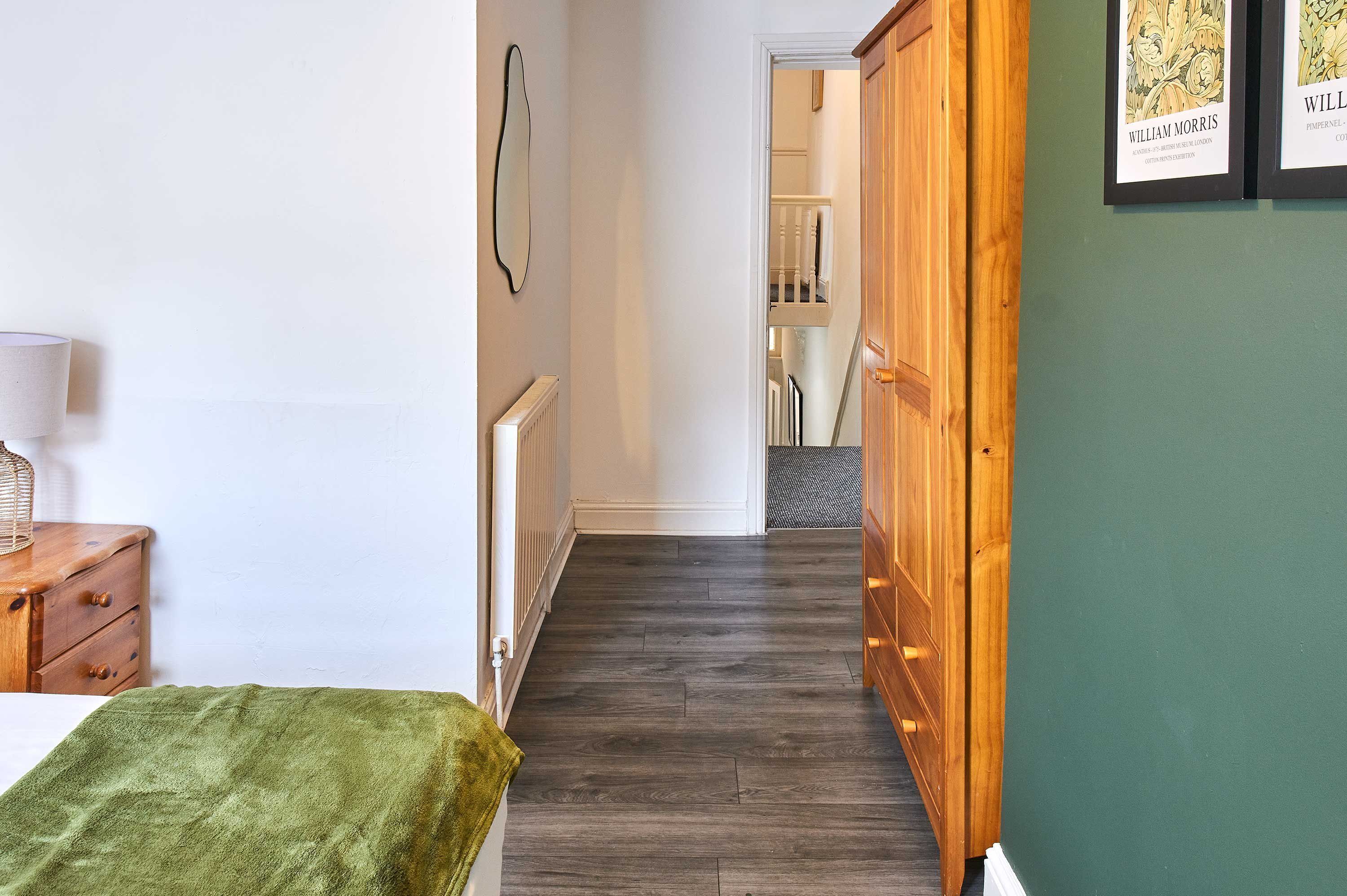 Un couloir avec un plancher en bois, un mur vert et une armoire en bois.