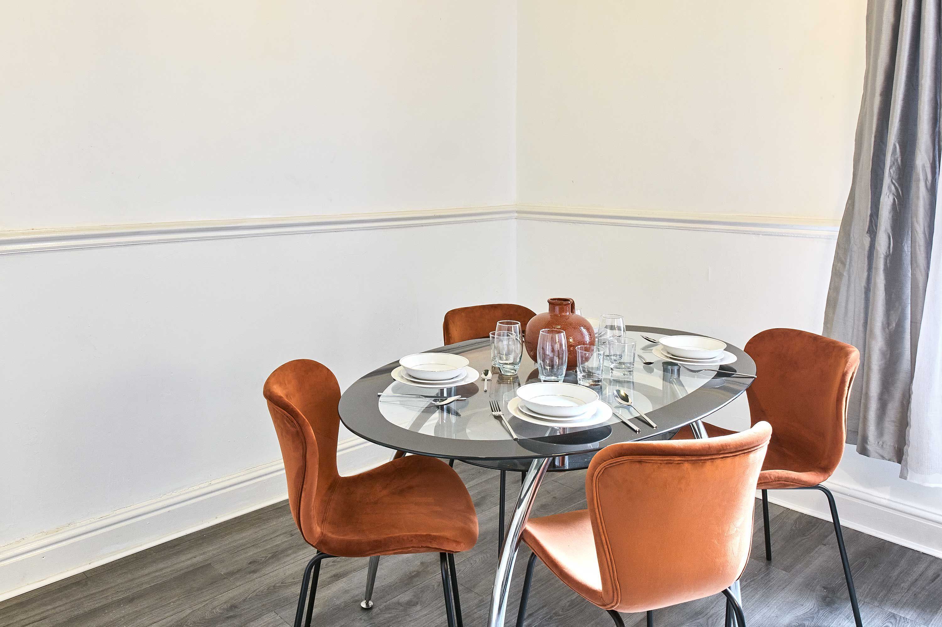 Une table de salle à manger ronde, entourée de quatre chaises, mise avec des assiettes, des verres et des couverts.