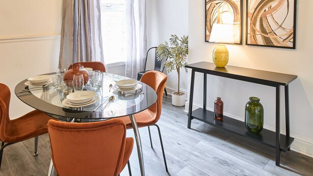 A dining area with a round glass table, orange chairs, and a black console table with decorative vases. - Host Stay Bishop House (Liverpool)
