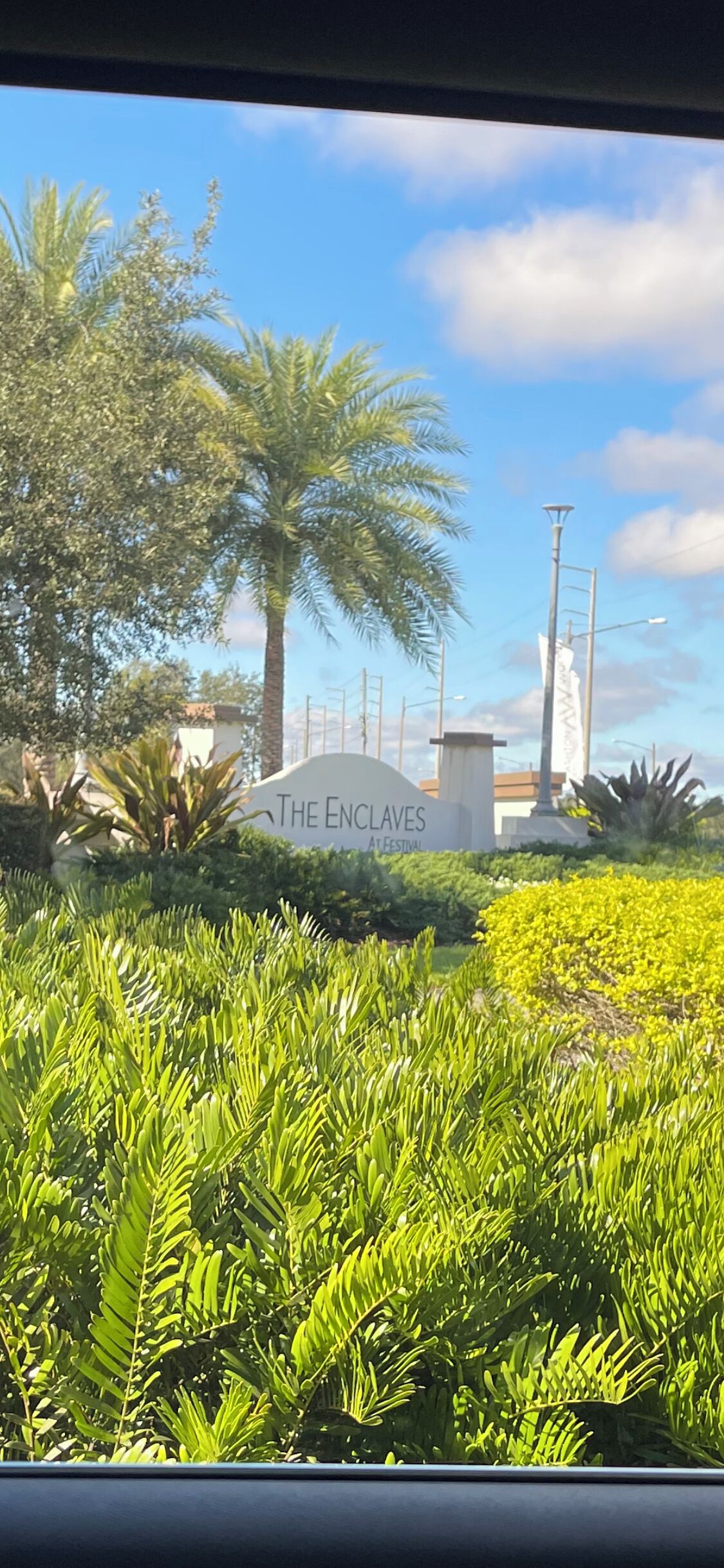Ein Schild für 'The Enclaves' mit üppiger Vegetation und Palmen im Hintergrund.