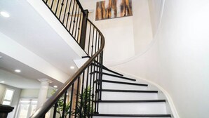 Un escalier en colimaçon avec des rampes noires et des murs blancs, menant à l’étage supérieur.