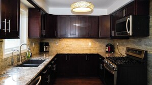 Une cuisine moderne avec des meubles de couleur bois foncé, un plan de travail en granit, une cuisinière encastrée et un luminaire suspendu.