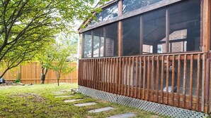 Une maison avec une terrasse en bois, un jardin clôturé et un arbre.