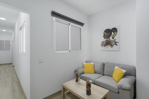 En moderne stue med en grå sofa, to gule puder, et træsofabord og et indrammet kunstværk på væggen.