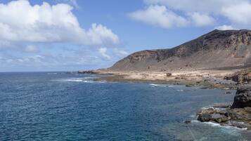 A coastal landscape with a rocky shoreline, a person fishing, and a distant mountain.