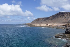 A coastal landscape with a rocky shoreline, a person fishing, and a distant mountain. - Vacation Apartment 'Isleta - Segundo B' with Wi-Fi (Las Palmas)