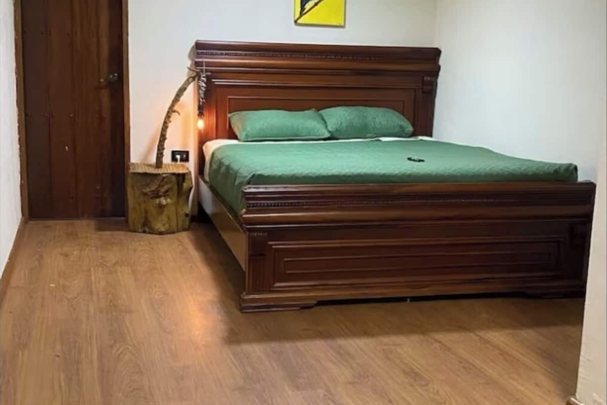 A bedroom with a wooden bed, a wooden floor, a wooden door, and a wall-mounted light fixture.