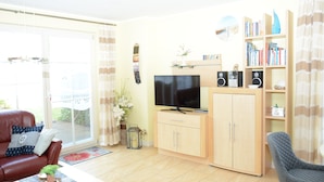 Una sala de estar con un sofá, una mesa de centro, un televisor, una estantería y un ventanal corredero al exterior.