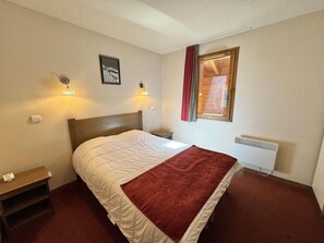 A bedroom with a bed, bedside tables, a radiator, and a window with curtains.