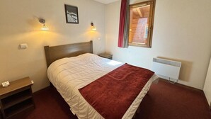 A bedroom with a bed, bedside tables, a radiator, and a window with curtains. - 3rd floor, swimming pool, terrace, parking, tv, ski locker, 58m², Vars (Vars)