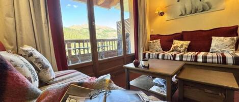 A cozy room with a sofa, a table, and a window with a view of hills.