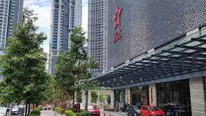 Una entrada de hotel moderna con un letrero llamativo, una zona de estacionamiento techada y edificios altos circundantes.