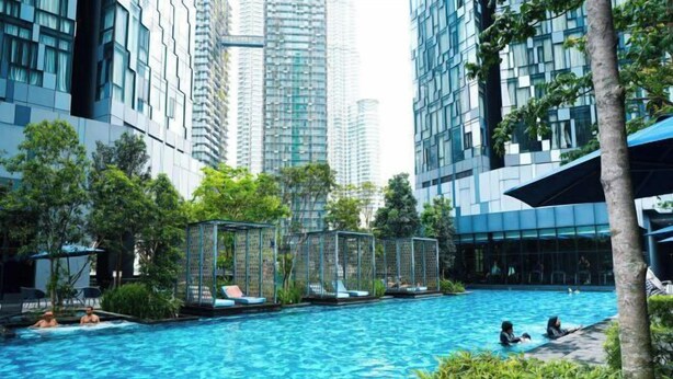 Una piscina rodeada de edificios modernos, árboles y sillas de descanso.