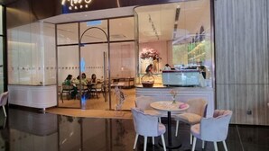 Miss O Cafe con un interior moderno, paredes de vidrio y una zona de estar con mesas y sillas.