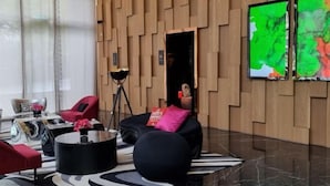 Un vestíbulo moderno con paneles de madera, un sofá de cuero negro con un cojín rosa, una mesa de centro negra y un sillón rojo.