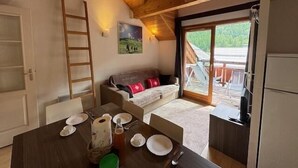 Ein gemütlicher Raum mit Holzbalkendecke, einem Esstisch gedeckt mit Tellern, Tassen und einem Wasserkocher, einer Couch mit Kissen und einem Bild an der Wand.