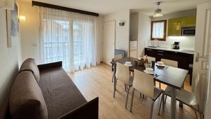 A compact living space with a sofa, dining table, chairs, a kitchenette, and a large window with sheer curtains. - 350m from ski slopes, 3rd floor, view ski slopes, balcony, 33m², Serre Chevalier (Saint-Chaffrey)