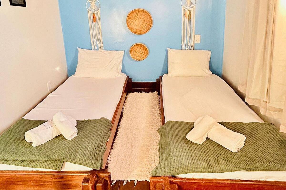 Ein Zimmer mit zwei Betten, Holzbalkendecke und einer blauen Wand mit gewebter Wandkunst.