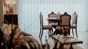 A dining area with a table set for four, surrounded by ornate chairs, a sofa, and a lamp on a side table.