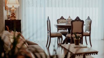A dining area with a table set for four, surrounded by ornate chairs, a sofa, and a lamp on a side table.