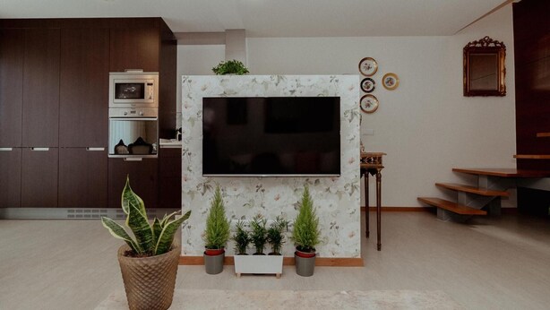 A modern living room with a flat-screen TV mounted on a wall, a built-in oven, and a staircase leading to an upper level.