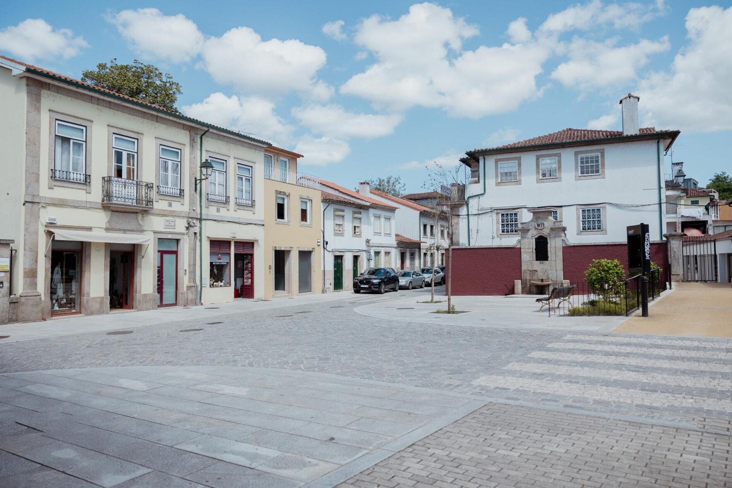 Une rue bordée d’immeubles, avec une zone pavée et des voitures garées.