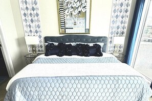 Quarto de hotel com uma cama, mesa de cabeceira, luminária, espelho e janela com vista.