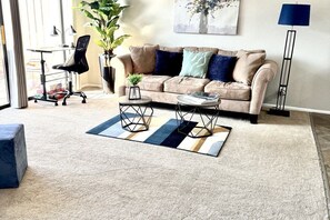 Sala de estar com sofá bege, mesa de centro, mesa lateral, planta em vaso e abajur.