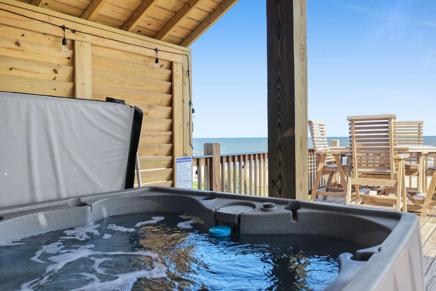 Een houten terras met een jacuzzi, houten stoelen en uitzicht op de oceaan.