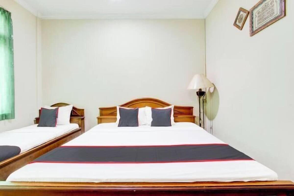 Ein Hotelzimmer mit zwei Einzelbetten, einem Holz-Kopfteil, einem Nachttisch, einer Lampe und einem gerahmten Zertifikat an der Wand.