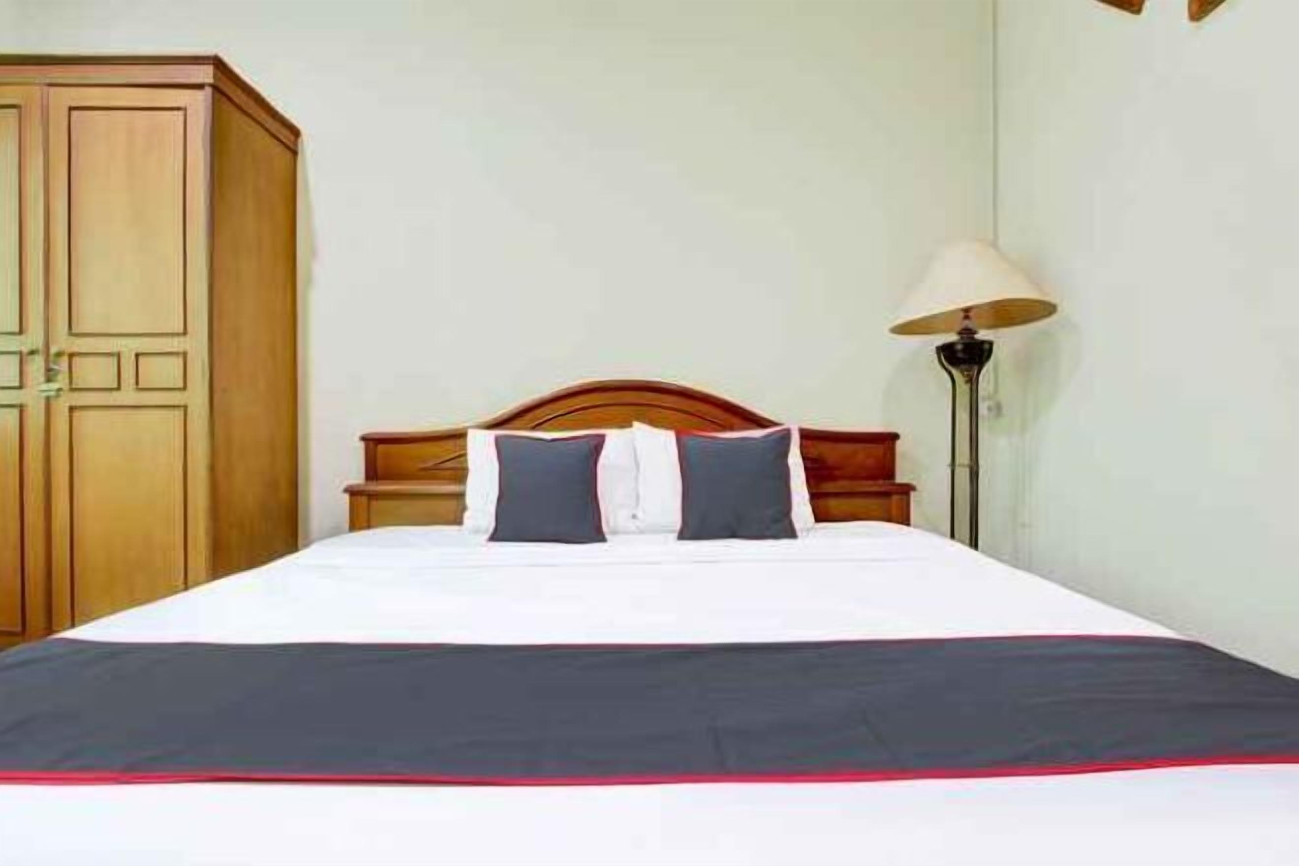 Una cama bien hecha con una colcha blanca y oscura, cabecera de madera y una lámpara en el lateral.