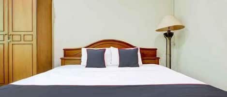 Una cama bien hecha con una colcha blanca y oscura, cabecera de madera y una lámpara en el lateral.