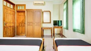 Una camera d'hotel con due letti, armadi in legno, una scrivania, una televisione e una finestra con tende.