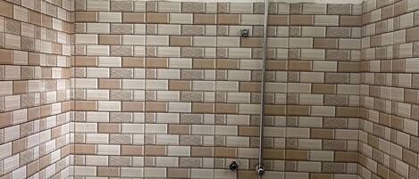 A bathroom with a tiled shower wall, a sink, and a handheld showerhead.