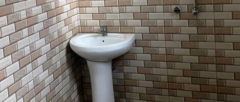 A bathroom with a tiled wall, a pedestal sink, and a shower.