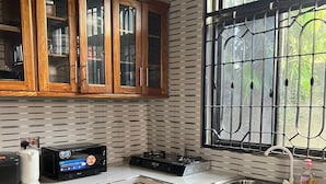 A kitchen with wooden cabinets, a microwave, a gas stove, and a window with metal bars. - Mashingo Homestay (Dar es Salaam)