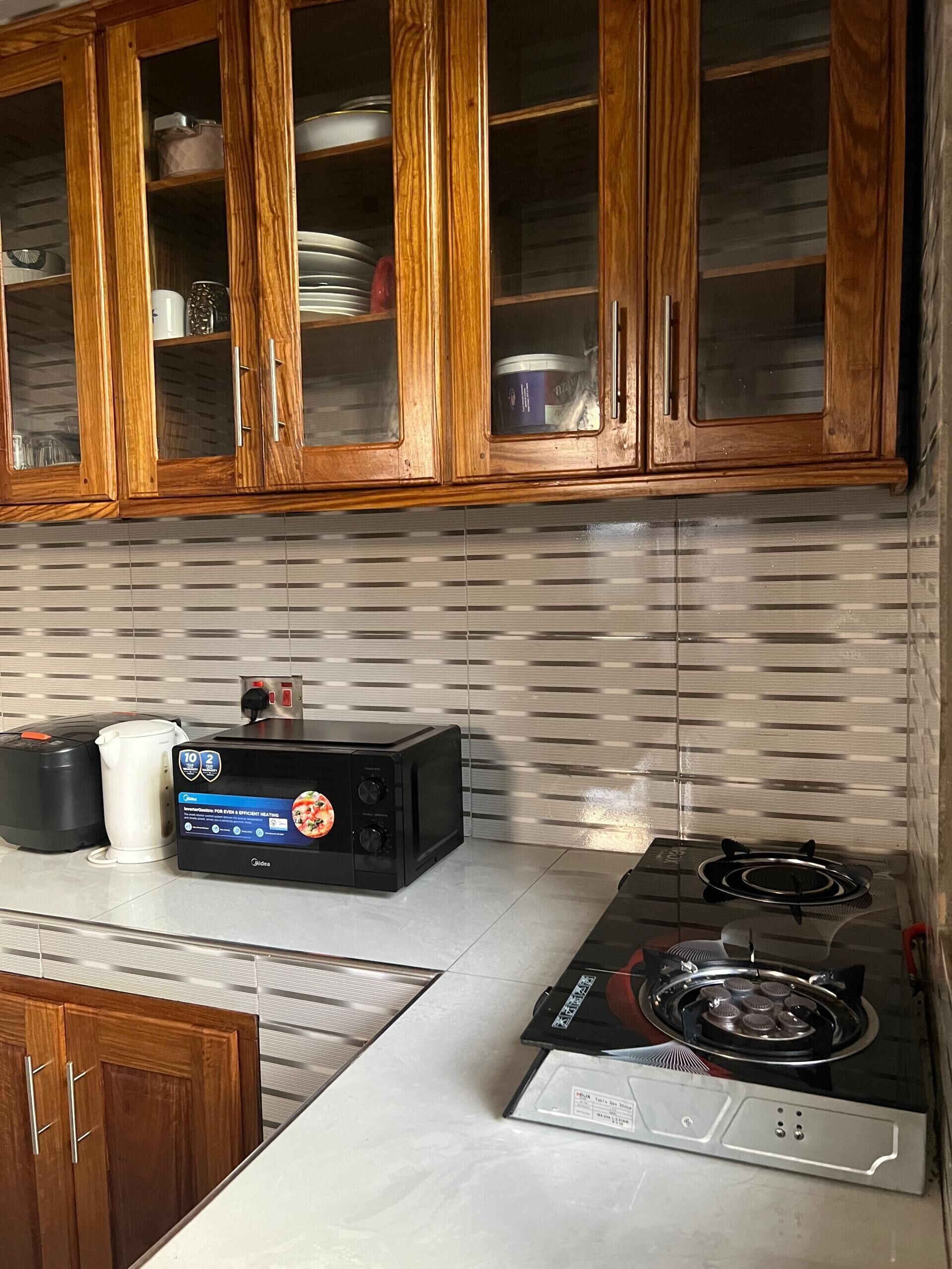 Una cocina con armarios de madera, microondas, hervidor y estufa a gas.