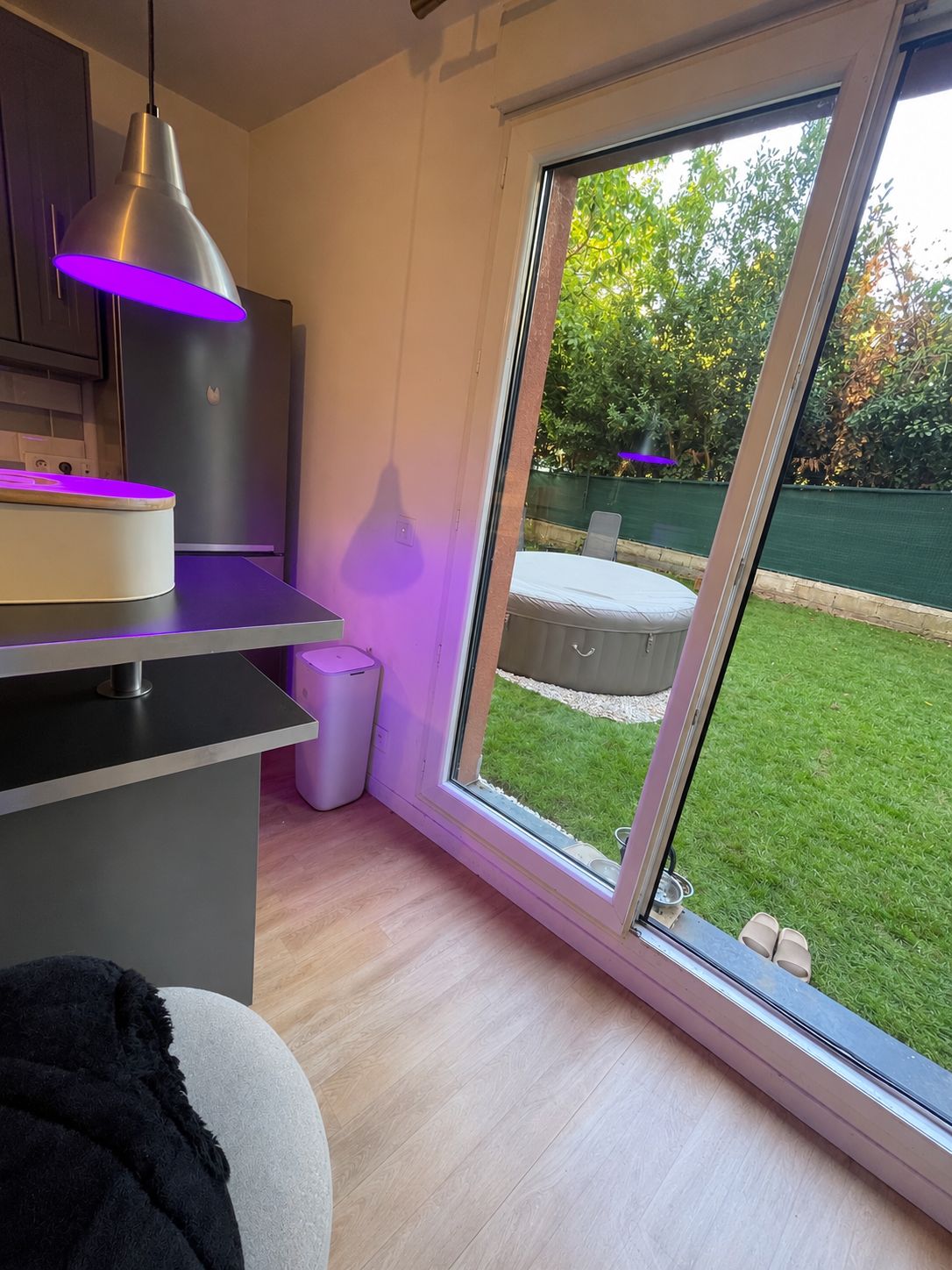 Une cuisine moderne dotée d’une grande fenêtre, d’un coin repas et d’un petit espace extérieur visible à travers la fenêtre.