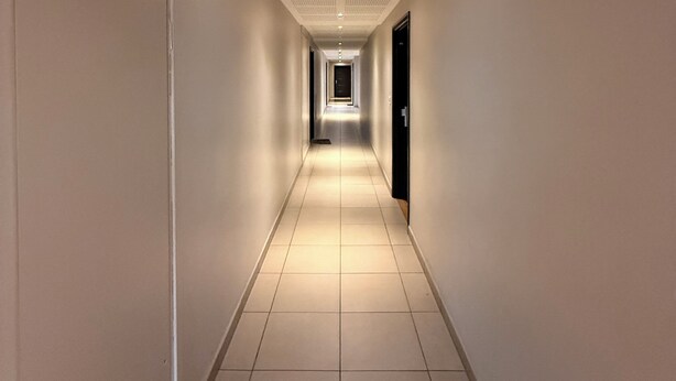 A long, narrow hallway with white tiled floors and walls, featuring a ceiling with a grid of small holes and recessed lighting. - Private room - Garden & terrace (Noisy-le-Sec)