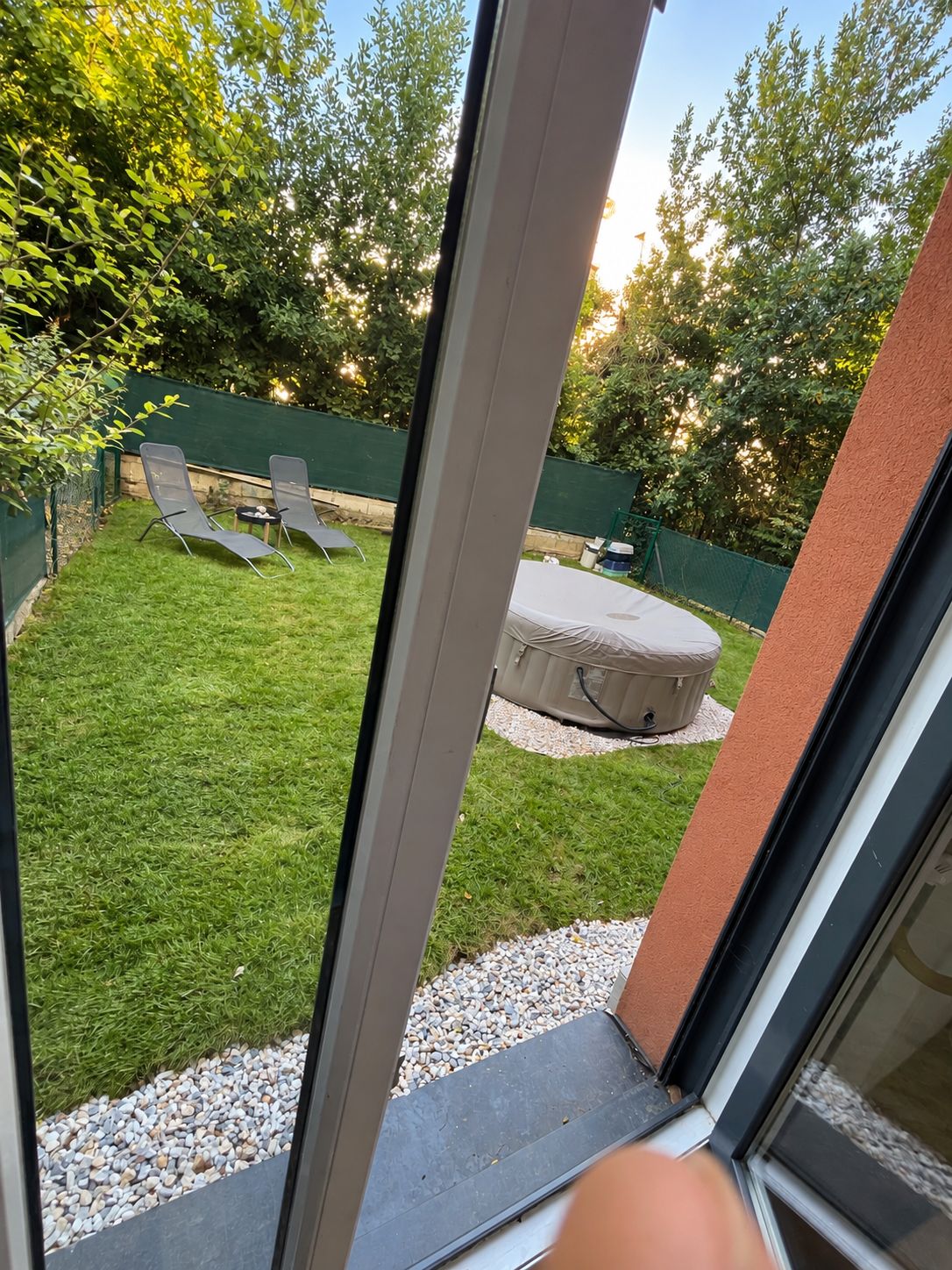 Een uitzicht op een achtertuin met gazon, twee lounge fauteuils, een kleine tafel en een overdekte zithoek.