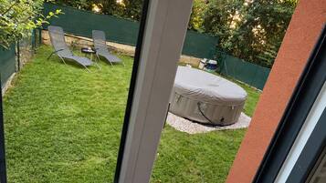 Een uitzicht op een achtertuin met gazon, twee lounge fauteuils, een kleine tafel en een overdekte zithoek.