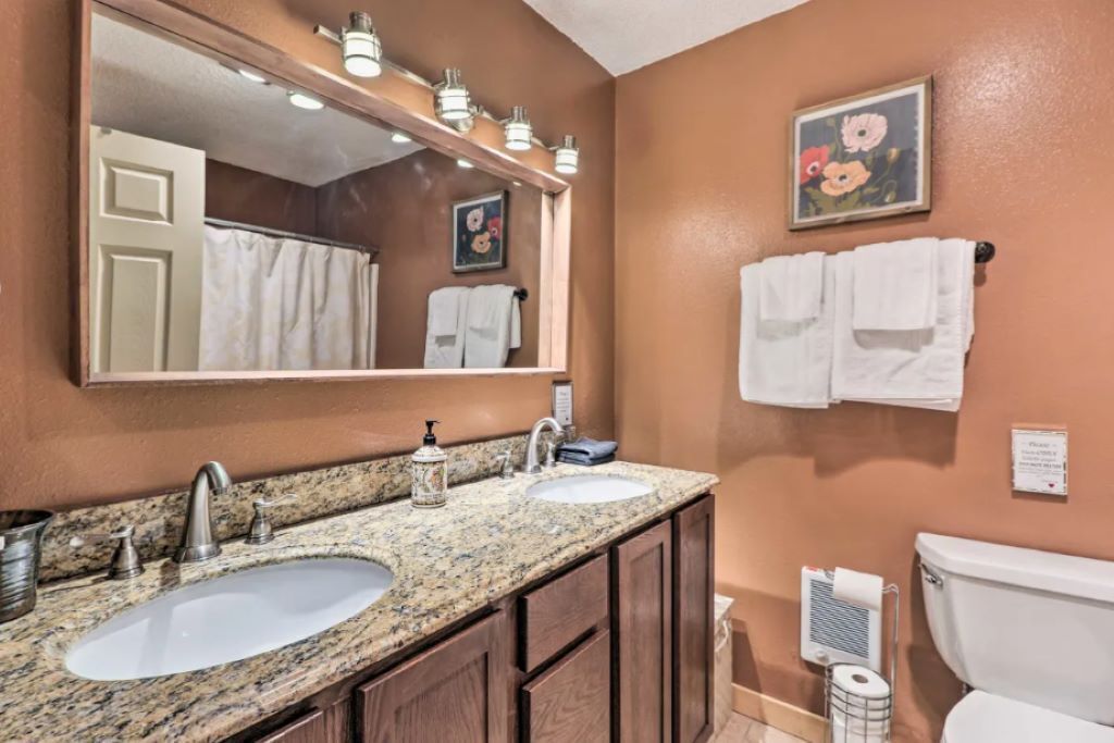 A bathroom with two sinks, a large mirror, and a toilet.
